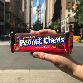 Hand holding a Goldenberg's Peanut Chews candy bar in a city street location