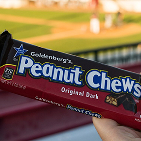 Hand holding a Goldenberg's Peanut Chews candy bar at a baseball park